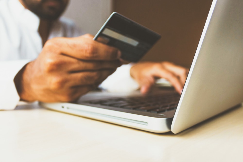 man holding credit card while typing on laptop computer