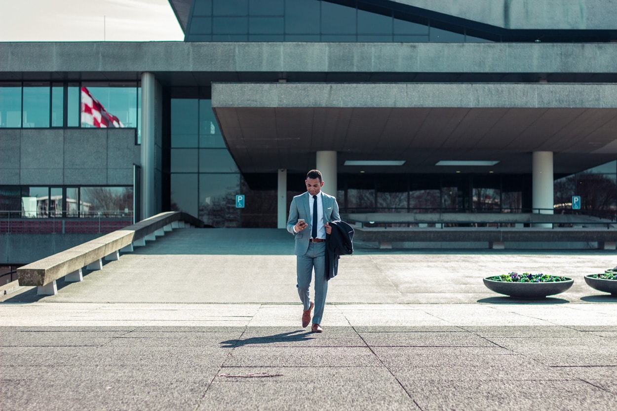 man in suit walking holding black coat and smartphone